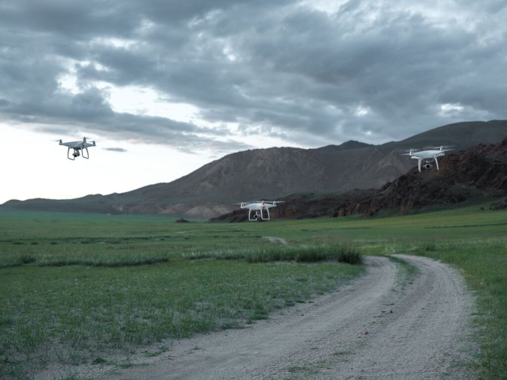 Aerial drones hovering over a picturesque landscape with fields and mountains under a cloudy sky.
